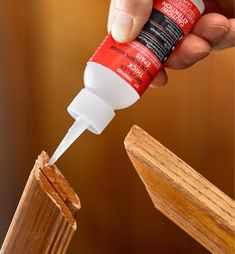 a hand holding a bottle of glue over a piece of wood