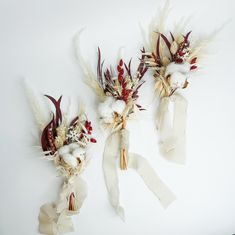 three dried flowers with ribbons tied to them on a white surface, one is red and the other is yellow