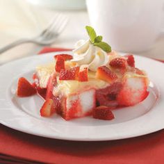 a piece of cake with strawberries and whipped cream on top sitting on a plate