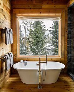 a bath tub sitting under a window next to a wooden wall and floor covered in snow