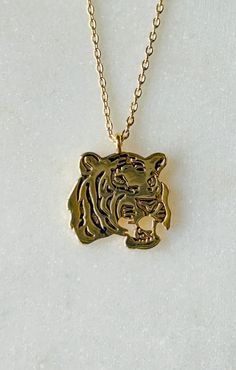 "Unleash your wild side with this stunning 14k gold dipped tiger charm necklace. Crafted with meticulous attention to detail, this necklace captures the strength and beauty of the majestic tiger. The tiger charm, with its intricate features and fierce expression, hangs gracefully from a delicate gold chain, creating a captivating and stylish accessory. Whether you want to channel your inner strength or simply adore these magnificent creatures, this necklace is a perfect addition to your jewelry collection. Let the power and elegance of the tiger grace your neckline and make a bold statement wherever you go. -14k Gold Dipped * Brass Casting * Lead & Nickel Free ◾ MEASURES * Necklace Length: 16.5\" plus 2\" adjustable chain * Pendant Width: 0.55\" * Pendant Height: 0.50\"  * Closure: Lobster Tiger Pearl Necklace, Tiger Bracelet Gold, Gold Lion Pendant Jewelry, Tiger Gold Pendant, Lion Pendant, Tiger Head, Etsy Bridesmaid Gifts, Gold Dipped, Dainty Necklace