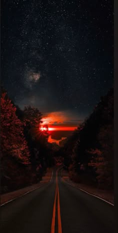 an empty road at night with the sun setting in the distance and stars above it