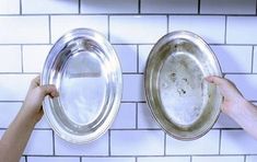 two hands holding silver dishes in front of white tiled backsplashes on a wall