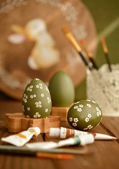 two green eggs sitting on top of a wooden table next to markers and paintbrushes