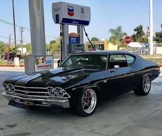 an old black car parked in front of a gas station with no one around it