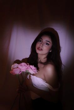 a woman holding a bouquet of flowers in front of a dark background with light coming through the curtain