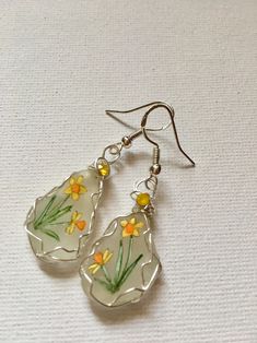 two glass dangles with yellow flowers are hanging from silver earwires on a white surface