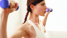 a woman holding two blue dumbs in her right hand and looking at the camera