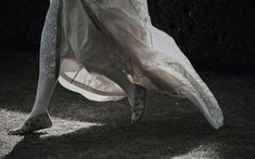 a woman is walking in the grass with her dress flowing over her body and shoes on