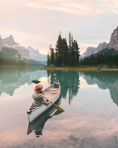 a person sitting in a canoe on a lake with mountains in the background and trees around