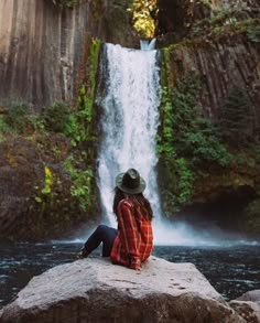 a woman sitting on top of a rock next to a waterfall