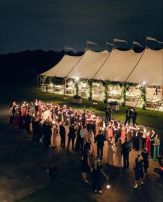 a group of people standing in front of a white tent at night with lit candles