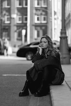 a woman is sitting on the curb with her hand under her chin