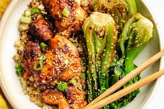 a white plate topped with meat and veggies next to chopsticks on a yellow table cloth