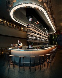 a bar with lots of stools in front of it and a man sitting at the bar