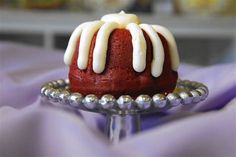 a red cake with white icing sitting on a silver plate next to purple cloth