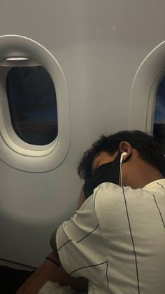 the man is sleeping on an airplane with ear buds in his ears and wearing a face mask