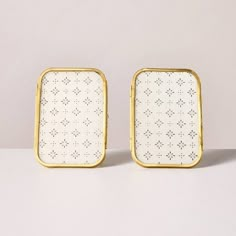 two white and gold square trays sitting on top of a table next to each other