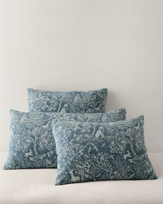 three blue pillows sitting on top of a white bed next to each other in front of a wall