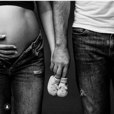 a man and woman holding hands while standing next to each other with baby shoes on their belly