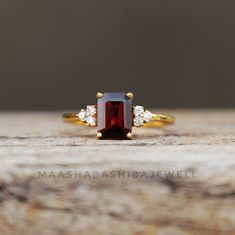 a close up of a ring with a red stone and two white diamonds on it