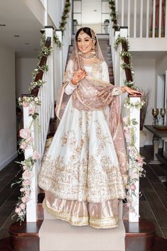 a woman in a white and gold bridal gown standing on stairs with flowers around her neck