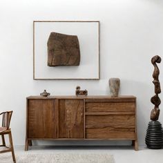 a wooden cabinet sitting in front of a mirror next to a chair and vase on top of a rug