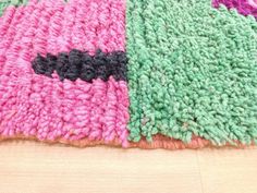 a pink and green rug on the floor next to a wooden table with a black cat