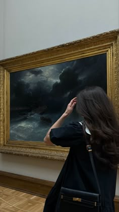 a woman standing in front of a painting looking up at it's frame with her hand on her head