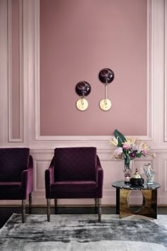 two purple chairs sitting next to each other in front of a wall with pink walls