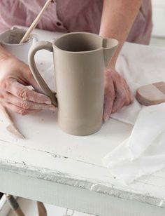 a woman is making a mug on a table with her hands resting on the handle