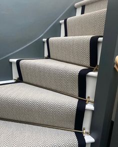 the stairs are lined with black and white chevroned carpeting, along with gold - plated handles