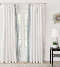 a white curtain with blue stripes hanging in front of a window next to a black table