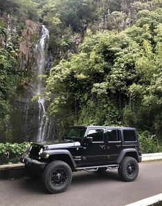 a black jeep parked in front of a waterfall on the side of a mountain road