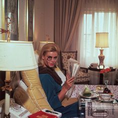 a woman sitting in a chair reading a newspaper and holding a cup with her right hand