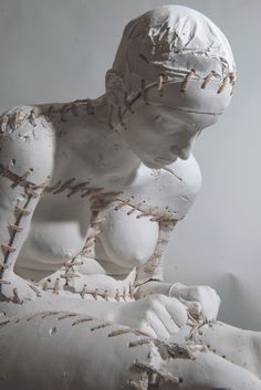 a sculpture of a person sitting on top of a white body with stitches all over it