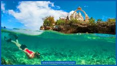 two people swimming in the ocean near a small island with a statue on it's side