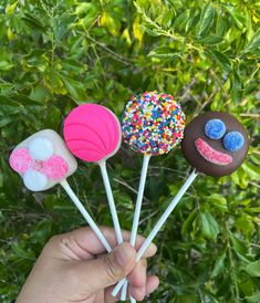 a hand holding four candy lollipops with sprinkles on them