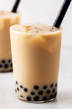 two glasses filled with drinks sitting on top of a table next to each other and one has a black straw in it