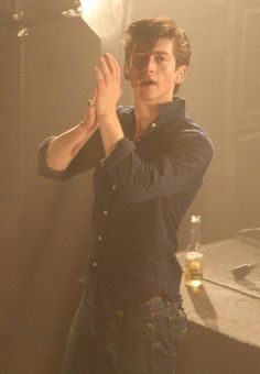 a young man standing in front of a table holding his hands up to the side