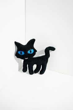 a black cat with blue eyes standing in front of a white wall