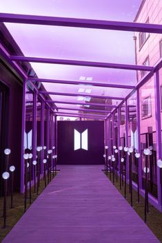 the walkway is lined with metal poles and purple lights are shining down on the building