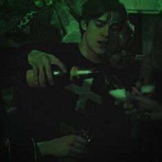 a man pouring wine into a glass in a dark room with other people around him