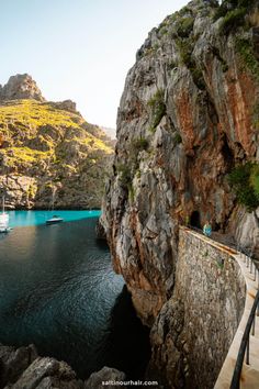 people walking along the side of a cliff next to a body of water with boats in it