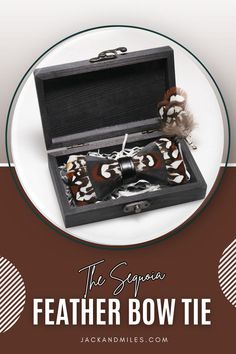 A unique feather bow tie with a bold black, brown, and white pattern, secured with a black leather band, nestled in an open black wooden box with shredded paper for presentation.