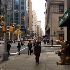 people are walking down the street in front of buildings and an animal statue on the sidewalk