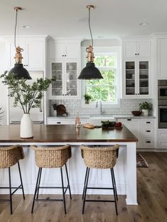 a kitchen with white cabinets and wooden counter tops next to two stools in front of an island