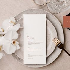 a place setting with white flowers and silverware on the table, next to a menu card