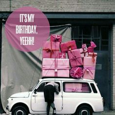 a white car with pink presents on top and a man standing next to it in front of a building