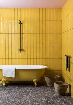 a bathroom with yellow tiles and a white bathtub in the center, next to two baskets on the floor